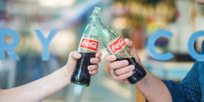Two people, toasting with glass bottles of Coke
