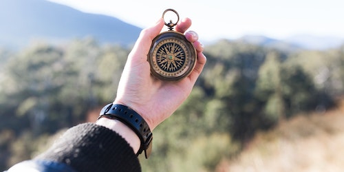 Photograph of a hand holding a compass in front of a blurred landscape