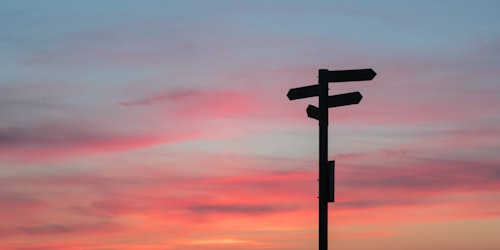 A wooden signpost against a gradient sunset