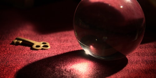 Crystal ball next to gold key on red table cloth